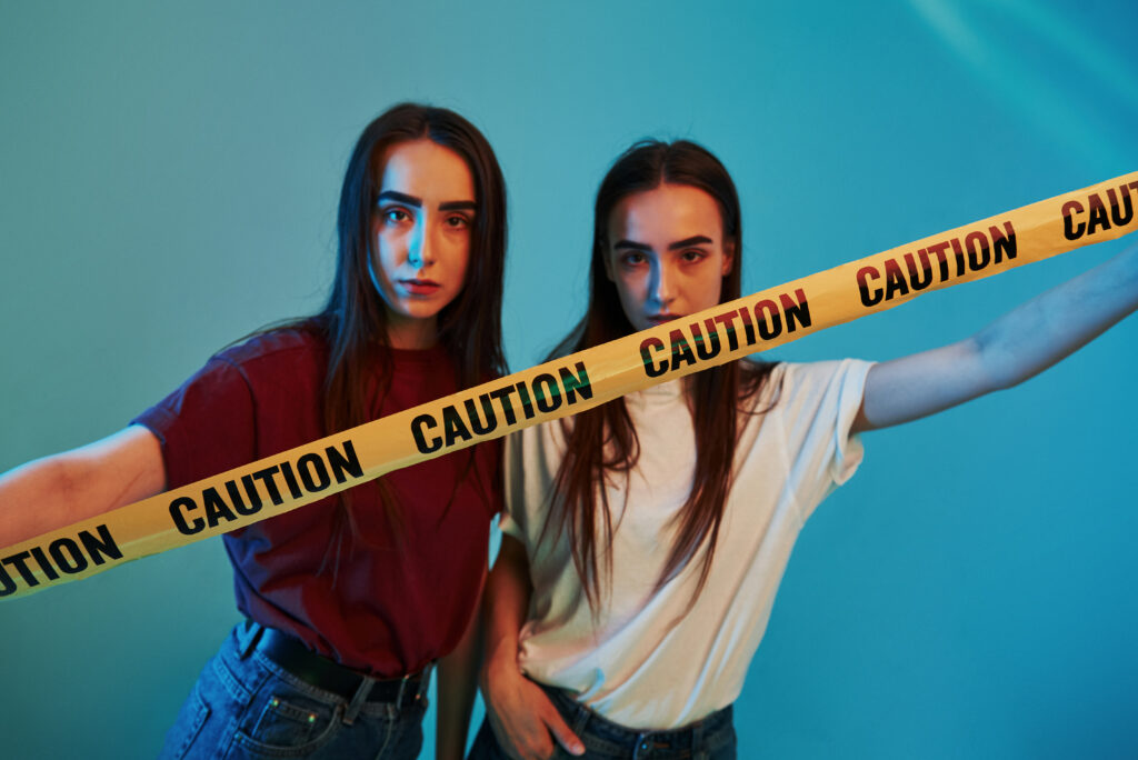 two girls holding a caution tape, symbolizing the "what are some warning signs of addiction" question