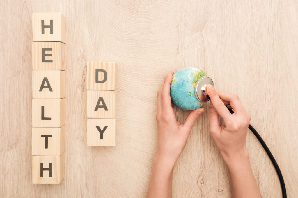 partial view of woman holding stethoscope, toy heart and cubes with health day lettering for World Health Day