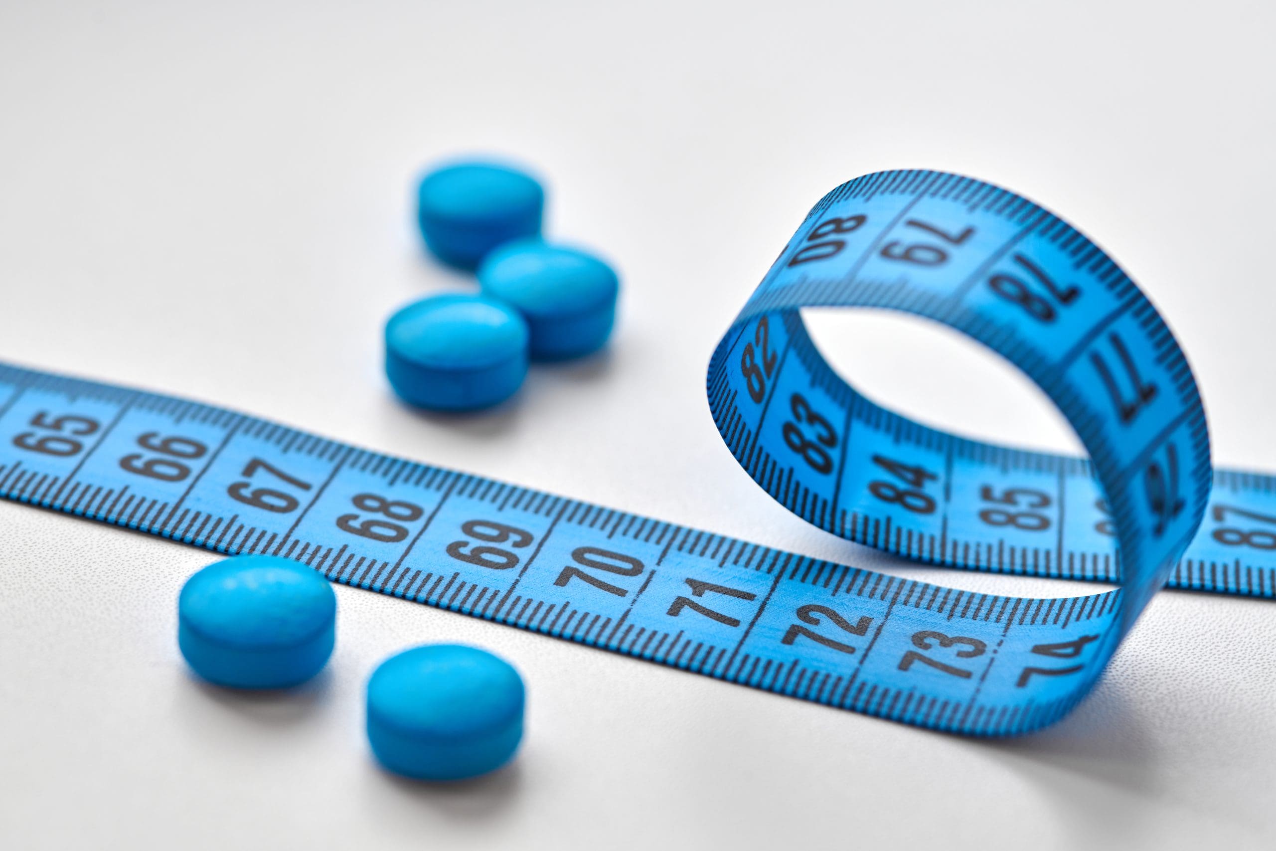 blue pills next to measuring tape to represent weight loss on adderall