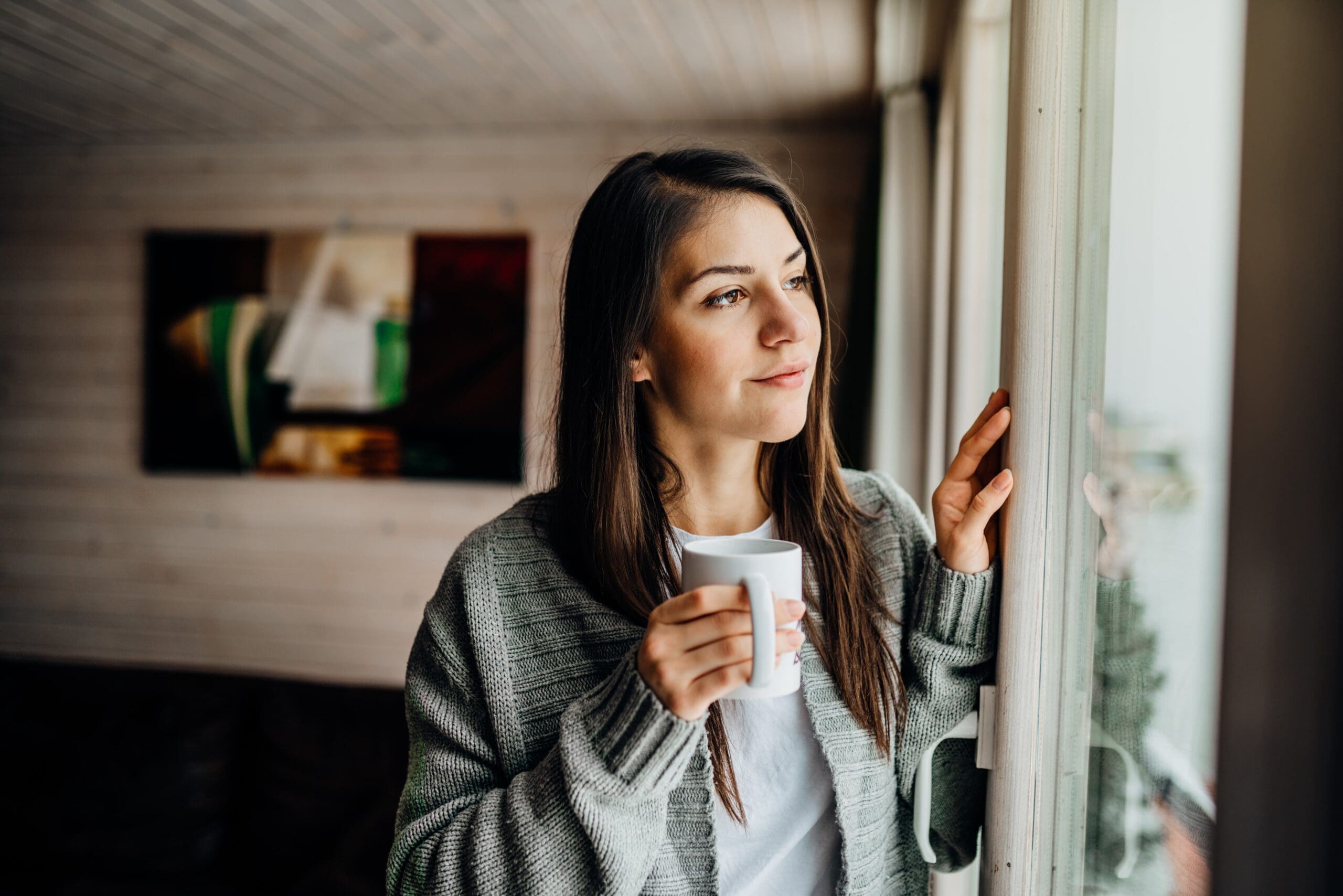 person looking out a window with a coffee mug, symbolizing peace and sobriety