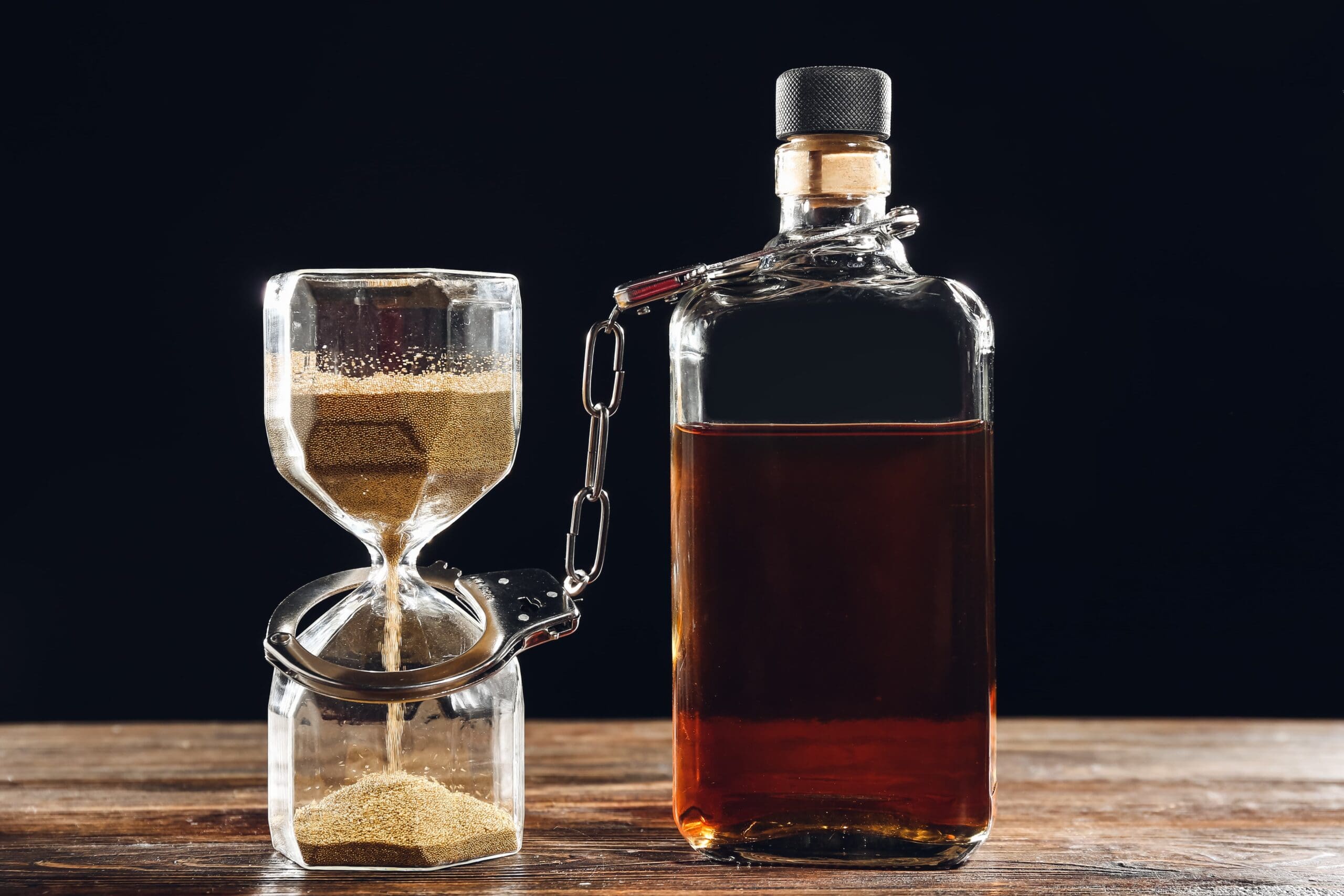 hourglass beside empty alcohol bottle representing time lost to addiction.